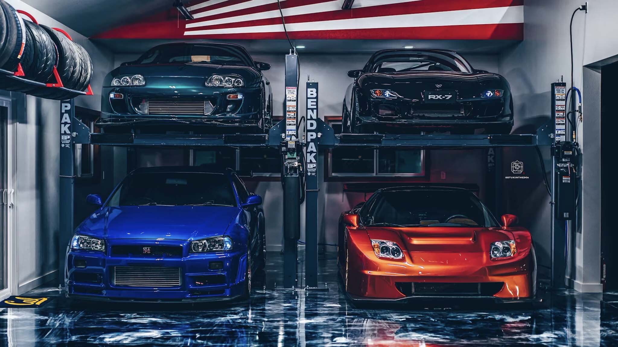Four iconic JDM sports cars displayed on lifts in a modern garage